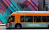 A bright orange Metro bus with a banner that says "Everyone on this bus is fighting climate change" in front of a brightly pa