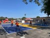 Kids and adults in bright orange shirts playing at two pickleball courts in a large asphalt schoolyard