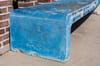 A concrete bench with the 1984 logo and Olympic logo painted blue and covered with graffiti on a sidewalk