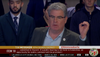 Councilmember Tim McOsker speaks at an LA City Council meeting holding up a "zero" with his fingers