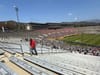A fan walks through rows and rows of empty seats at the Rose Bowl stadium as soccer players take the field