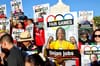 Signs that read Fair Games showing photos of workers are held up by a crowd in front of the LA Coliseum