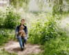 Melanie Winter, wearing a blue sweater and jeans, is holding her fuzzy pup on a rope swing in the vegetation of the LA River