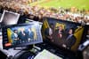 President Donald Trump in a red tie standing with FOX reporters shown on two video screens in the control room of an NFL game