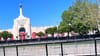 The LA Memorial Coliseum with the Olympic rings and the cauldron lit above surrounded by security fencing where a stadium worker is walking